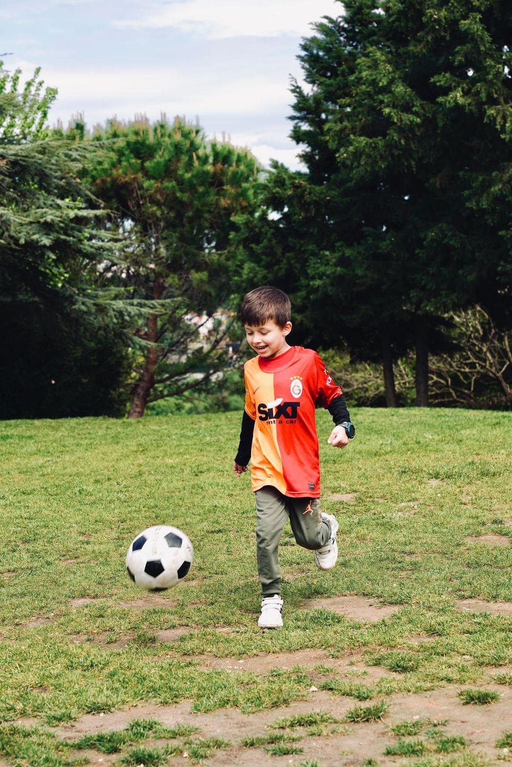 A little boy kicking a soccer ball in a green park