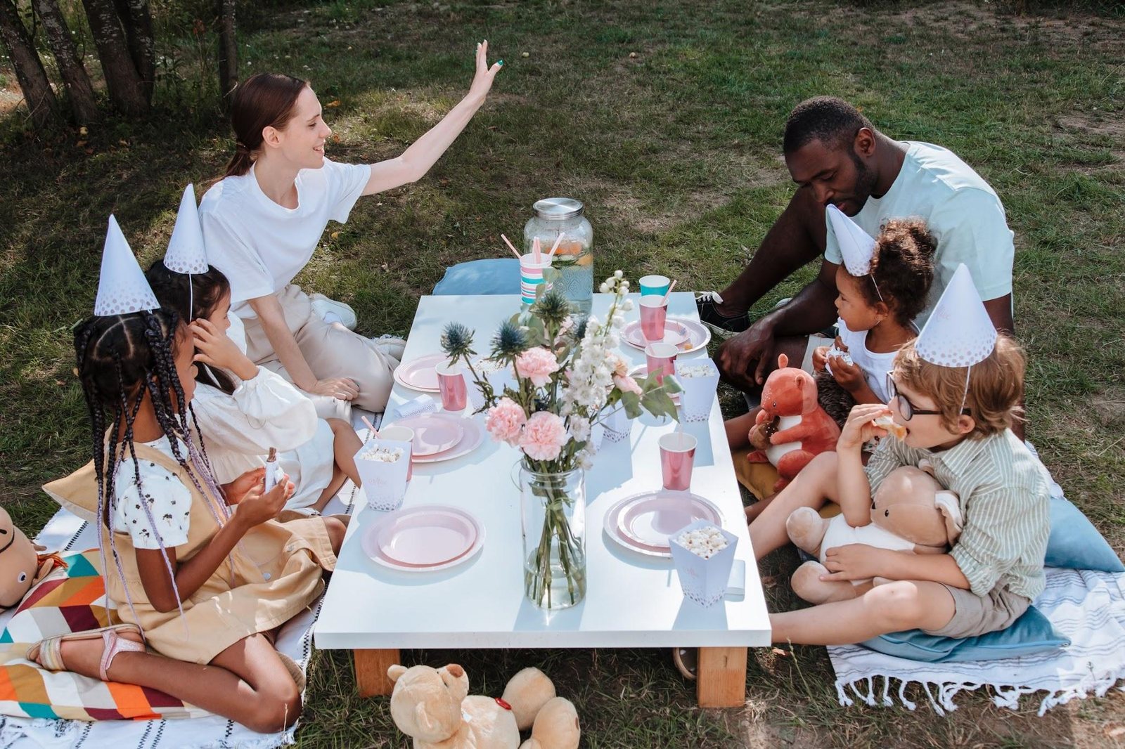 Kids at an outdoor birthday party sitting on grass with party hats and snacks